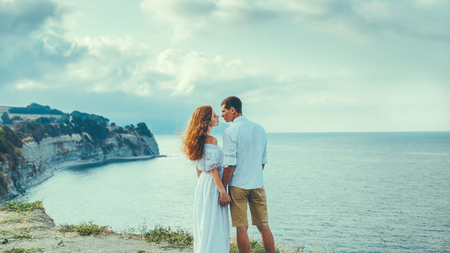 Couple Of Loving People, Young Man And Woman Standing On The Beach And Young Man And Woman Standing By The Sea And Kissing, Rear View. Enjoying Summer Together Conceptの写真素材