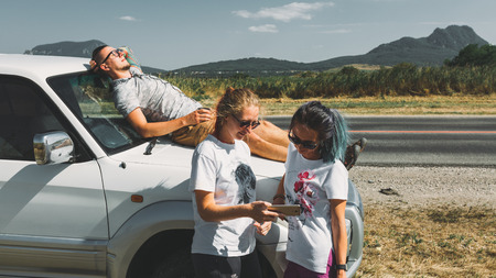 Three Friends Wanderer Searching Direction On Location Map On Smartphone, Two Girls And Guy Tourist Resting In Tripの写真素材