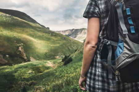 Unrecognizable Traveler Girl With Backpack Enjoying View Of Summer Mountains, Close-up Rear Viewの写真素材