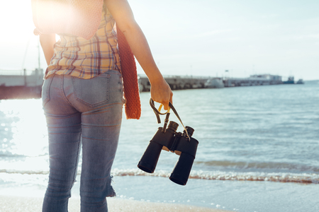 Young Woman With Binoculars In Hand Standing By The Sea And Enjoying View Of Nature, Rear Viewの写真素材