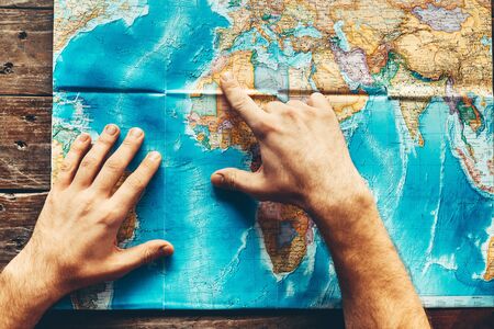 Mens Hands On A Paper Map Of The World Indicate The Final Destination, Top Viewの写真素材