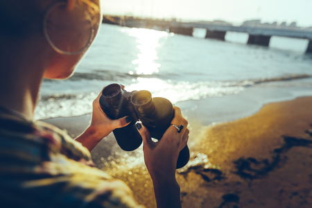Unrecognizable Young Girl Standing On The Shore And Holding Binoculars. Scout Wunderlast Travel Conceptの写真素材