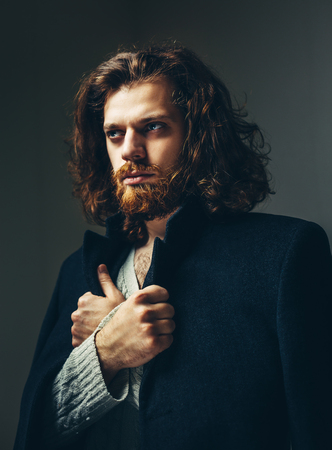 Portrait of a handsome man with a beard and long hair in a black coatの写真素材
