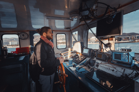 Young Capitan With Beard Stands At The Helm And Controls The Ship, View From Inside Captain's Cabinの写真素材