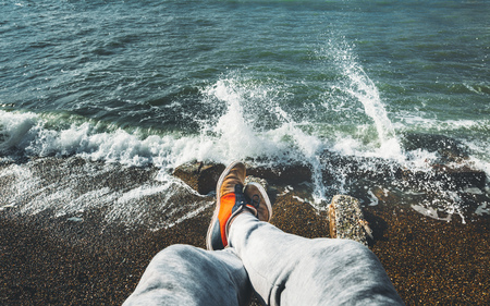Man Traveler Sits On Cliff Overlooking The Sea Surf Travel, Point Of View Shot. Lifestyle Adventure Vacations Conceptの写真素材