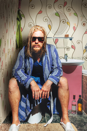 adult man with a beard, wearing glasses and a robe, sits in the bathroom and looks into the camera. Artistic Creative Portraitの写真素材