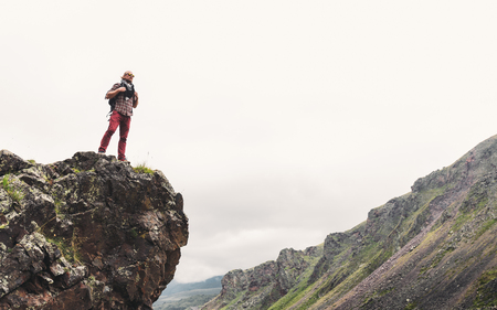 Young Man With Backpack Standing On Rocky Stone In Summer Mountains And Looking Into The Distance. Wanderlust Travel Journey Conceptの写真素材