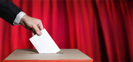 Voter Holds Envelope In Hand Above Vote Ballot On Red Background. Freedom Democracy Conceptの写真素材
