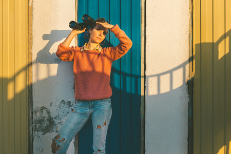 Young Beautiful Girl Stands Near Colorful Wall With Binoculars In Hand And Staring Into The Distance. Scout Travel Conceptの写真素材