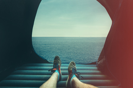 Legs Man In A Tourist Tent on picturesque summer seascape. View of the feet, point of view shotの写真素材
