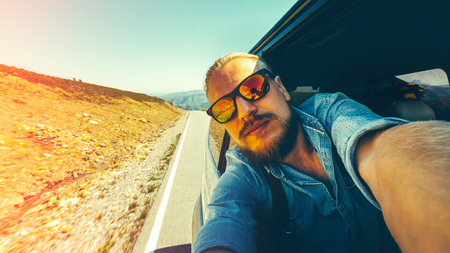 Travel Vacation Holiday Concept. A handsome young man doing selfie during a road adventure sitting in the car.の写真素材