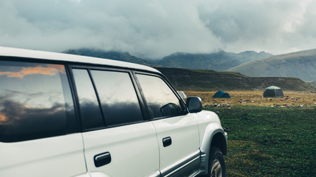 Road adventure concept. Car standing near tents on a camping in the summer mountains and cloudsの写真素材