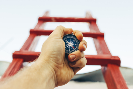 Motivation, search and movement towards the goal. Self-realization concept. A man with a compass is looking for direction on the background of a red staircaseの写真素材