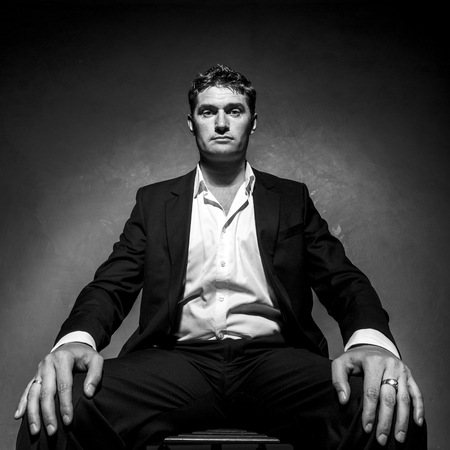 Handsome man in a business suit sitting on a chair, black and white portrait, low angle shotの写真素材