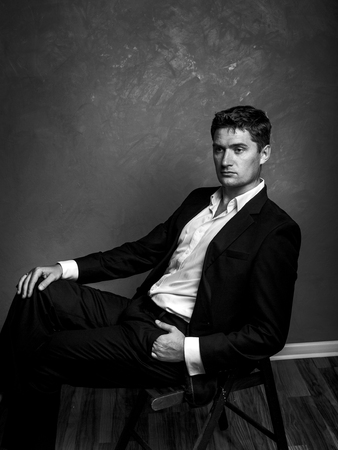 Handsome man in a business suit sits on a chair and looks away, style fashion black and white portraitの写真素材