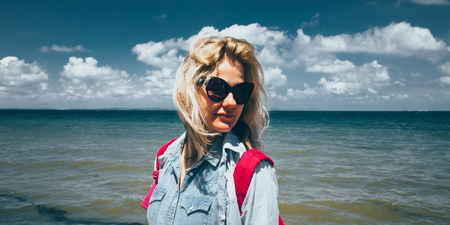 Girl traveler with a backpack stands on the background of the sea and enjoys the beautiful scenery. Concept of travel, adventure, tourism on vacation.の写真素材