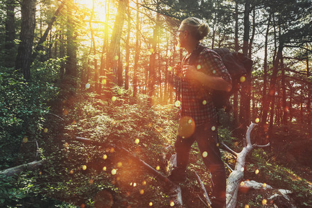 Traveler man with  backpack walks through the forest and enjoys the view of the sun. Concept of adventure, hiking and discoveryの写真素材