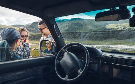 Three friends near the car discuss the route in the journeyの写真素材