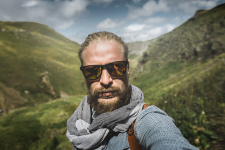 Global Travel Concept. Young Hiking Man In Sunglasses Take A Selfie On A Background Of A Mountain Landscapeの写真素材