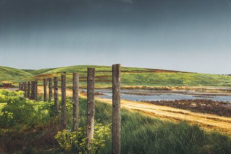 Endless fence of the countryside near the sea. Picturesque colorful landscape against mountains, sky and rural meadowの写真素材