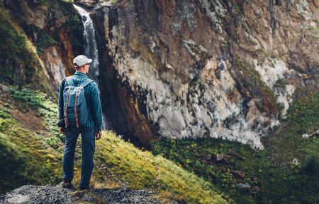 Young Traveler Man Standing On Top Of Cliff In Mountains And Enjoying View Of Nature, Rear View with copy-spaceの写真素材