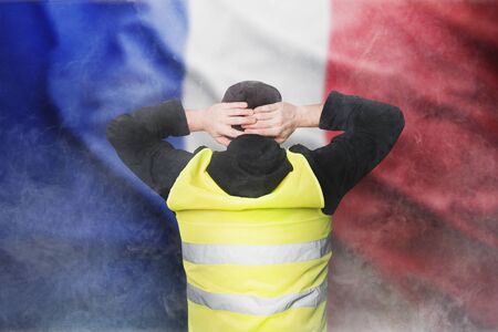 Yellow vests protests. A young man stands with his back and holds his hands on his head as a sign of obedience. The concept of revolution and protest, the struggle for equal rights, the electoral movementの写真素材