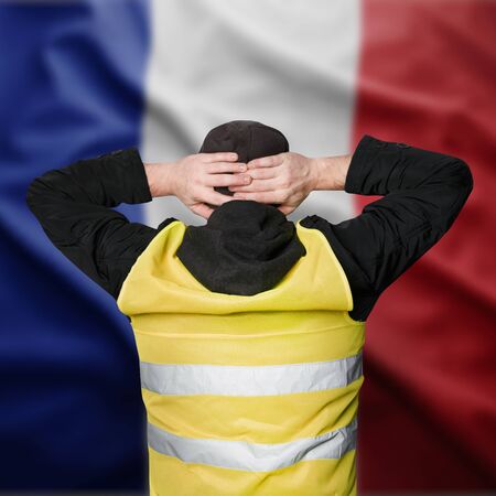 Yellow vests protests. A young man stands with his back and holds his hands on his head as a sign of obedience. The concept of revolution and protest, the struggle for equal rights, the electoral movementの写真素材
