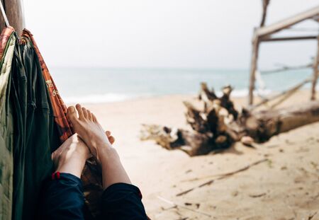 Summer vacation concept. Unrecognizable womans legs in hammock on beach against background of sea. Happiness, tourism, relaxation, enjoymentの写真素材