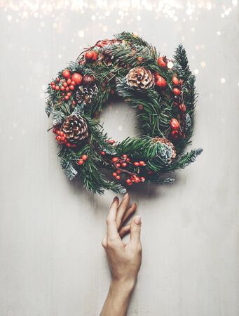 Home decoration for winter holidays. Female hand carefully touches a Christmas wreath on white background with lights, wooden top view. New year conceptの写真素材