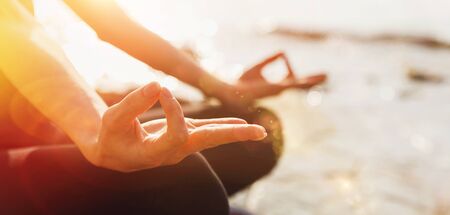 Unrecognizable Woman practicing yoga lesson in lotus position doing Ardha Padmasana exercise, closeup of body part with sunny light. Concept of biohacking, meditation, breathing, mental health. Banner with text spaceの写真素材
