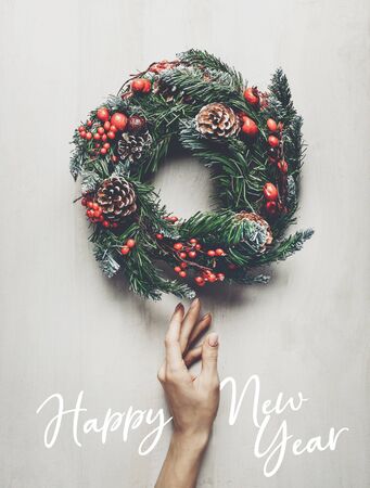 Home decoration for winter holidays. Female hand carefully touches a Christmas wreath on white background, wooden top view. New year conceptの写真素材