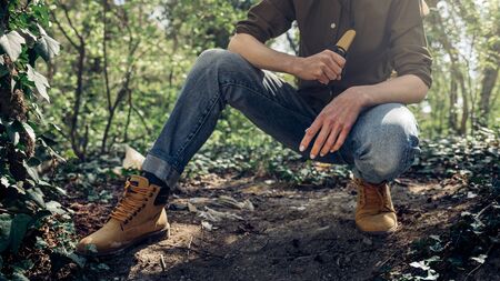 Survival Bushcraft Forest Concept. Unrecognizable woman sitting and holds neck knife in handsの写真素材