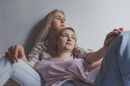 Portrait of young gay couple, girls lesbian sitting and hugging on background white wall. Concept of love, gay marriage and prideの写真素材