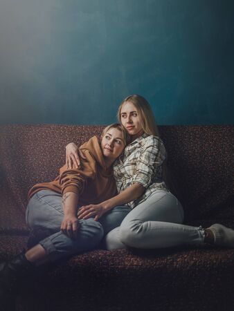 Portrait of young gay couple, girls lesbian sitting and hugging on background of blue wall. Concept of love, gay marriage and prideの写真素材