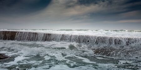 White foam waves roll through breakwaterの写真素材