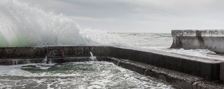 Waves crash against breakwater, forming splashesの写真素材