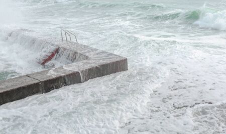 Waves crashing on breakwater with red stairs, turning into milk foamの写真素材
