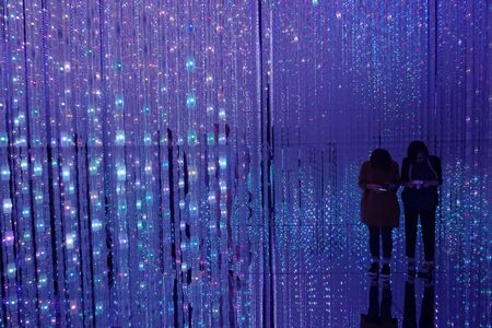 young people take selfies in the mirror floor. Silhouettes of people behind a curtain of electric blue garlands. Floor mirrorsの写真素材