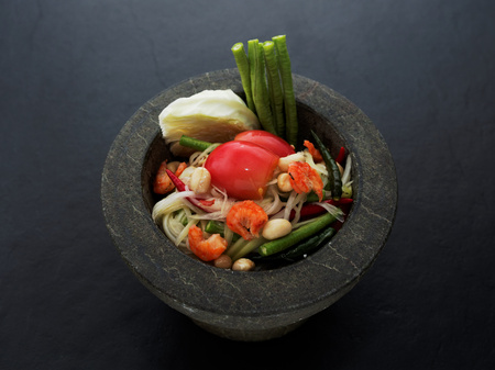 Thai green papaya salad (Som tum) in granite mortar on dark backgroundの写真素材