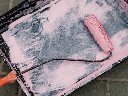 Paint roller in a black tray painting pink color on the street backgroundの写真素材