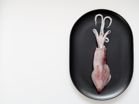Raw squid or cuttlefish on black oval plate isolated on white backgroundの写真素材