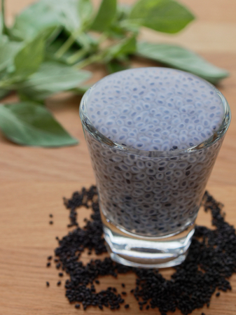 Swelled sweet basil or sabja seeds in shot glass with dried seeds and leaves on wooden backgroundの写真素材