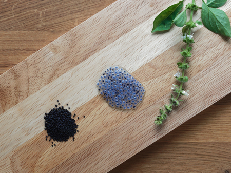 Dried and swelled sweet basil or sabja seeds with flower and leaves on wooden cutting board over wooden backgroundの写真素材