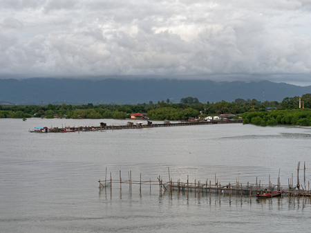 Scenery evening view of Leam Sing estuary or river mouth, where Chanthaburi river meet the sea, with small pier and boat for local fishery and mountain in the backgroundの写真素材