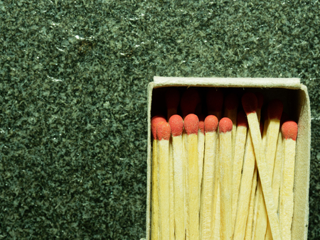 A group of wooden match sticks with red head in match box over black or dark granite texture with concepts of energy, old fashion, vintage, and retroの写真素材