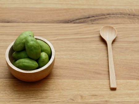 A group of green hog plums fruit in wooden bowl with wooden spoon over bright wooden background with concepts of wellness and healthy as they are rich in natural antioxidants, vitamins and mineralsの写真素材