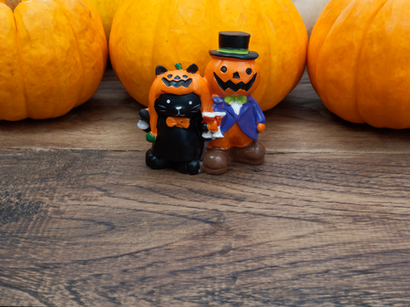 Orange miniature ceramic pumpkin guy with black cat with three orange pumpkins on the background over dark wooden surface with copy space used in Halloween, still life, kitchen, and decorationの写真素材
