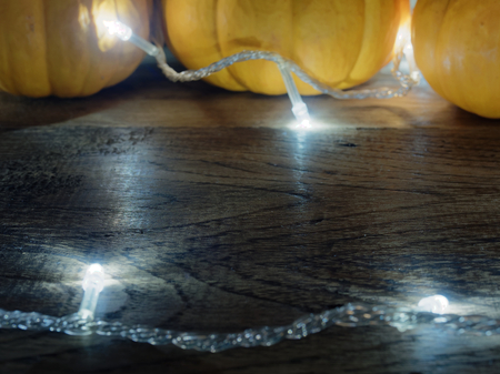 White decoration lights with yellow and orange pumpkins over dark wooden surface with space used as background, wallpaper, or backdrop in Halloween, festival, ornament and decoration themeの写真素材