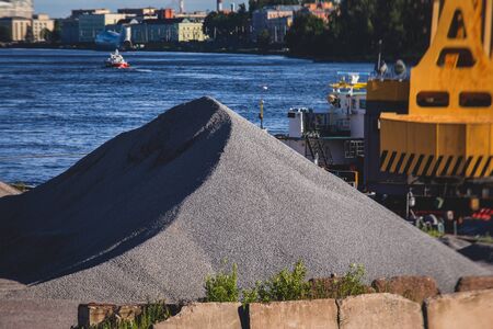 Bulk-handling crane unloading sand, road metal and gravel from cargo vessel ship, heavy vehicle and portal crane loader working with bulk materials in dock terminal の写真素材