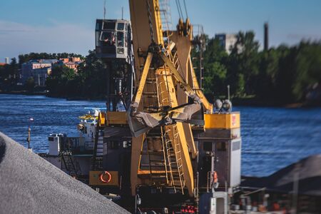 Bulk-handling crane unloading sand, road metal and gravel from cargo vessel ship, heavy vehicle and portal crane loader working with bulk materials in dock terminal の写真素材